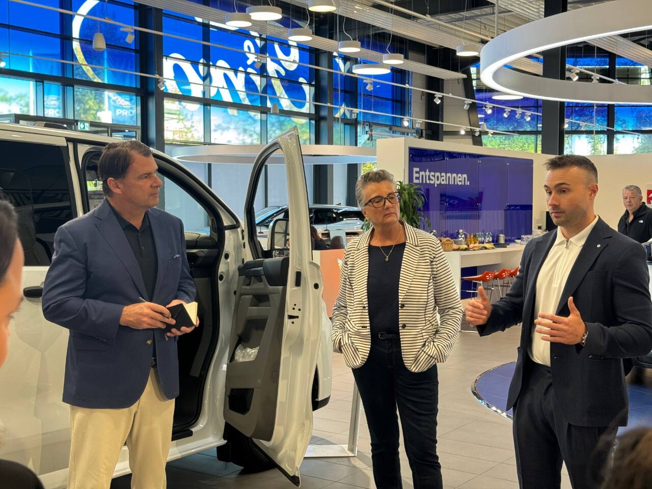 A candid photo of a group of people talking near a white vehicle in a show room.